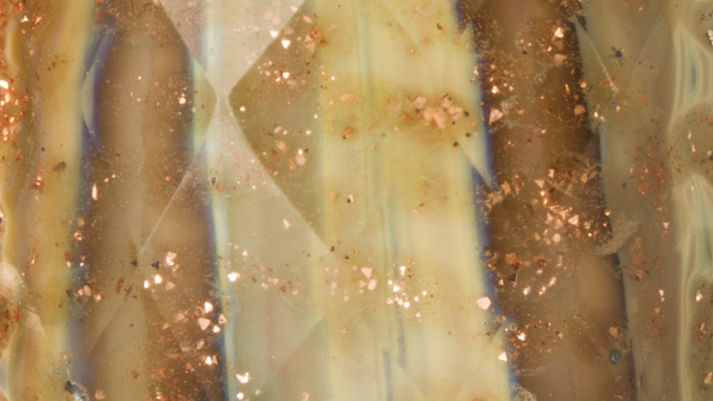 Nærbillede af Trolllneads Gyldne Minder. Den facetterede glaskugle er designet med nuancer af dulche de leche og honning. Når lyset danser på overfladen, træder glimmer og strejf af blå frem. 