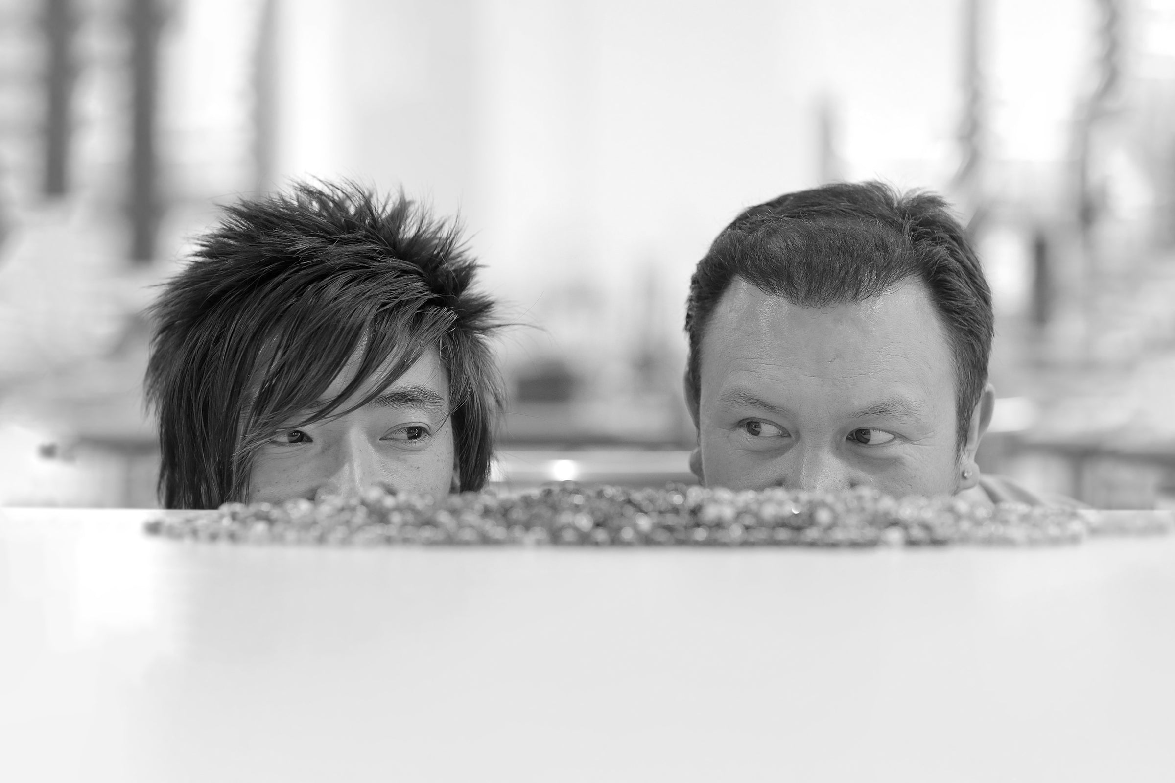 Two designers peeking over a railing with a blurred outdoor background